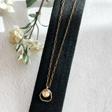 gold fill metal disc cupping two freshwater pearls with sterling open link on gold fill chain on black background with flowers to one side.