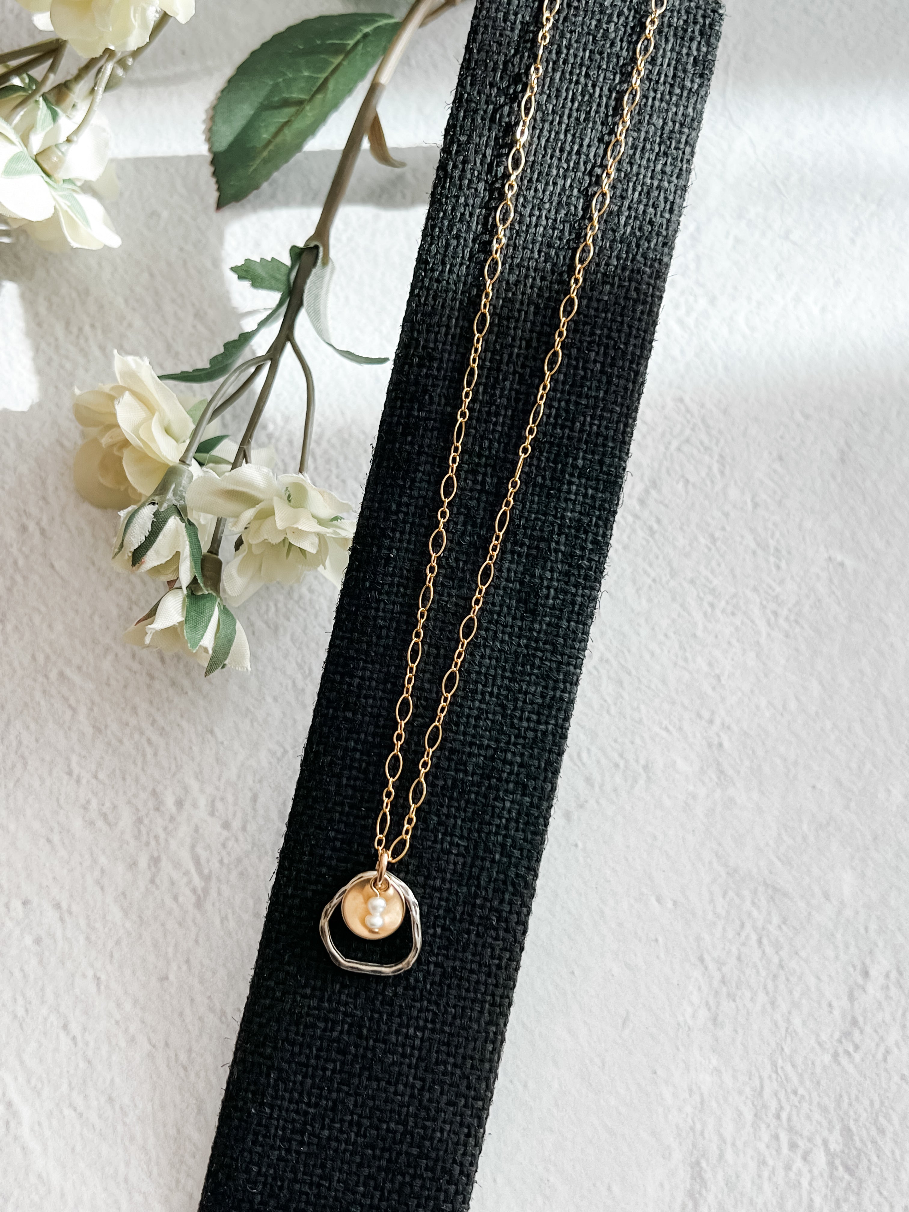 gold fill metal disc cupping two freshwater pearls with sterling open link on gold fill chain on black background with flowers to one side.