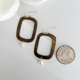 Dawn Carlson Designs textured bronze rectangular earrings with freshwater pearls displayed beside a US quarter coin, showing approximately 1.5 inch earring length