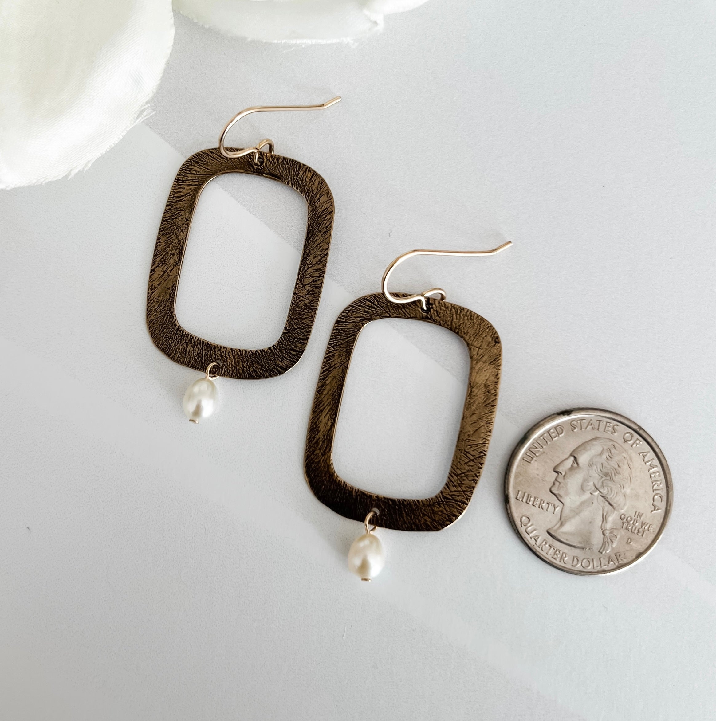 Dawn Carlson Designs textured bronze rectangular earrings with freshwater pearls displayed beside a US quarter coin, showing approximately 1.5 inch earring length