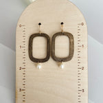 Handcrafted bronze rectangular hoop earrings with white freshwater pearl drops mounted on wooden measurement display, showing earrings measure approximately 2 inches in total length