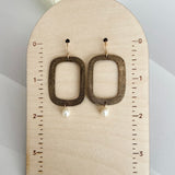 Handcrafted bronze rectangular hoop earrings with white freshwater pearl drops mounted on wooden measurement display, showing earrings measure approximately 2 inches in total length