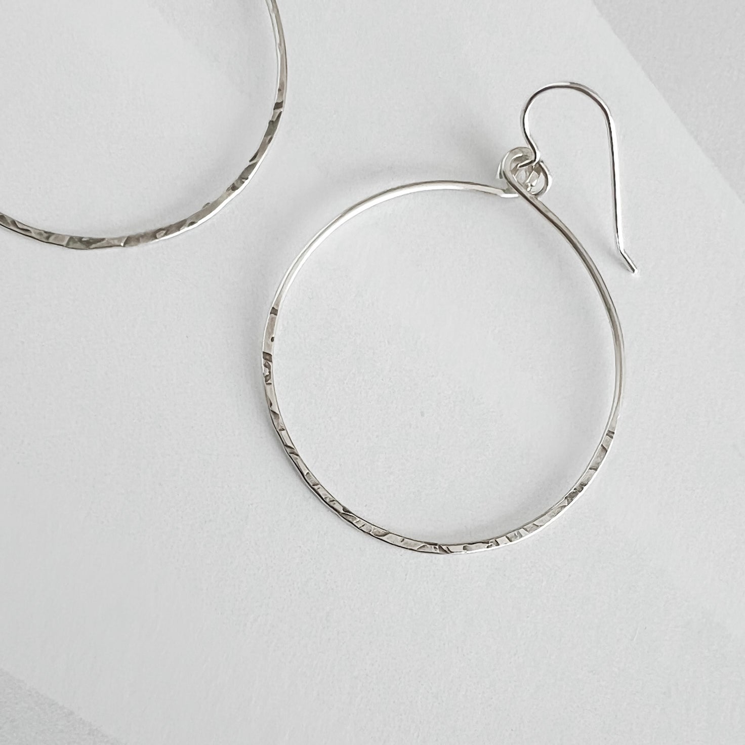 Close up of hammered sterling silver circle hoop earring showing textured finish and ear wire detail