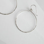 Close up of hammered sterling silver circle hoop earring showing textured finish and ear wire detail