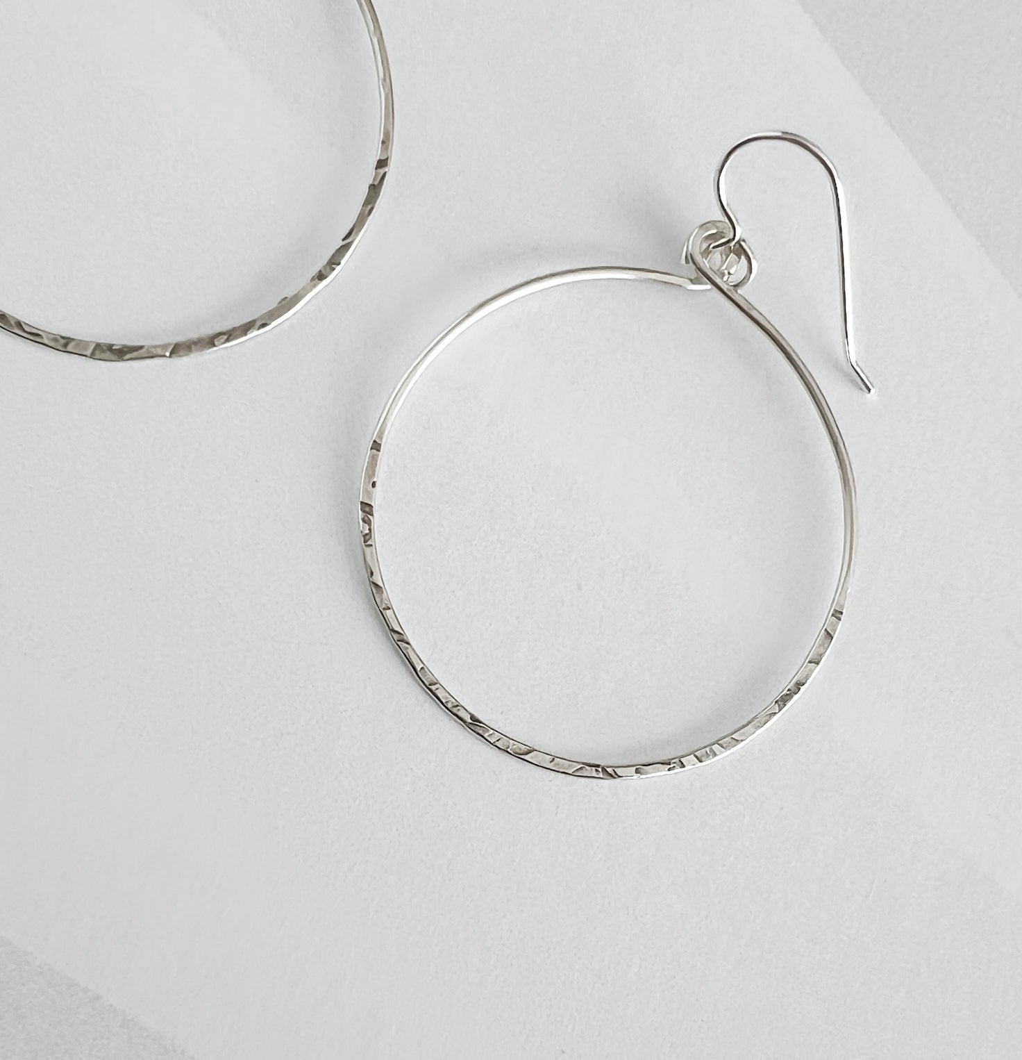 Close up of hammered sterling silver circle hoop earring showing textured finish and ear wire detail
