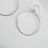 Close up of hammered sterling silver circle hoop earring showing textured finish and ear wire detail