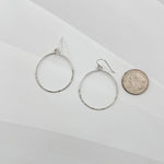Handcrafted sterling silver hammered circle hoop earrings displayed beside a US quarter coin, showing approximately 1.5 inch diameter, lightweight everyday hoops