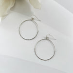 Silver hoop earrings on a white surface with flowers in the background