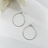Silver hoop earrings on a white surface with flowers in the background