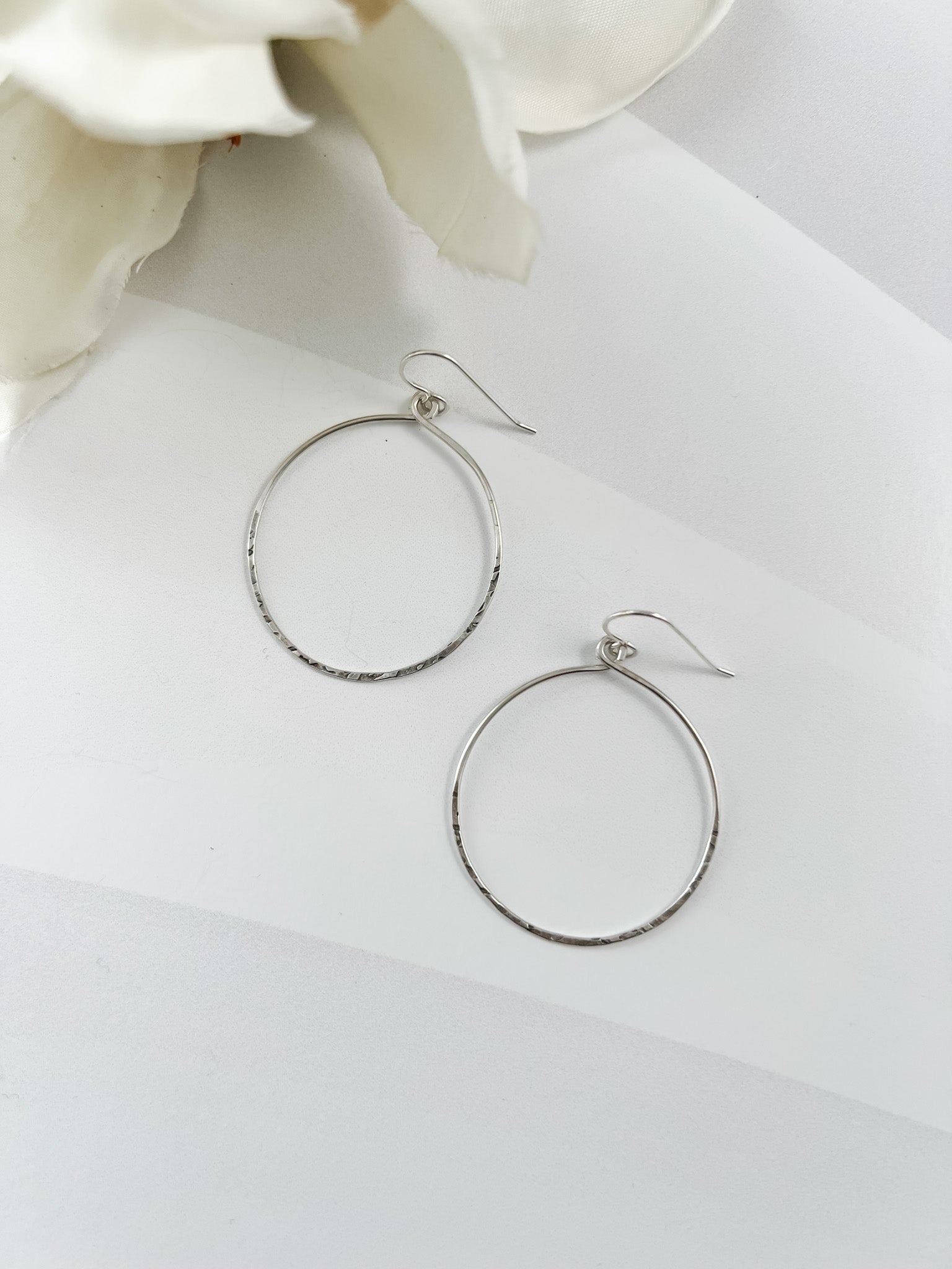 Silver hoop earrings on a white surface with flowers in the background