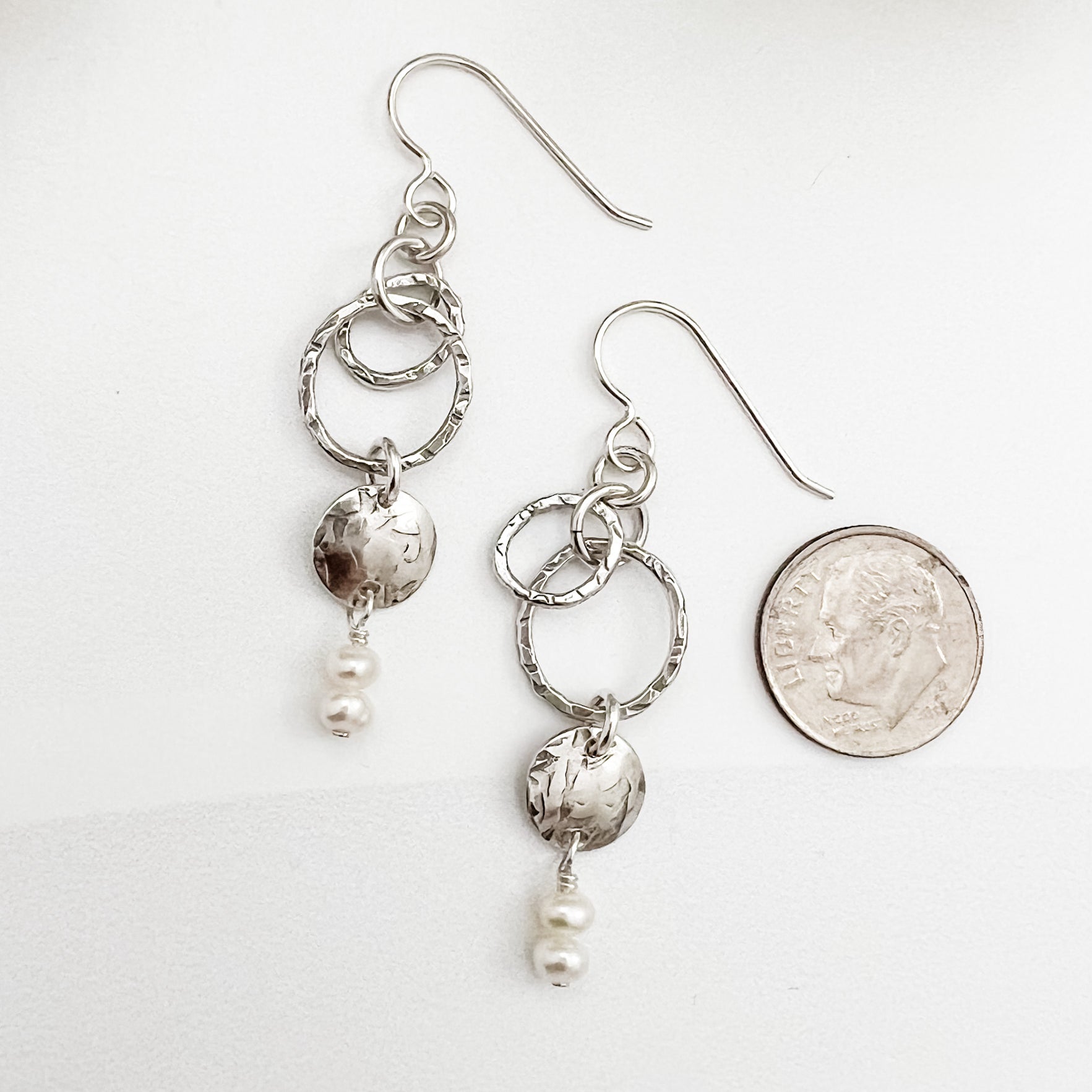 Sterling silver and pearl dangle earrings shown next to dime for scale, featuring textured hoops and luminous freshwater pearl drops, handmade by Dawn Carlson Designs