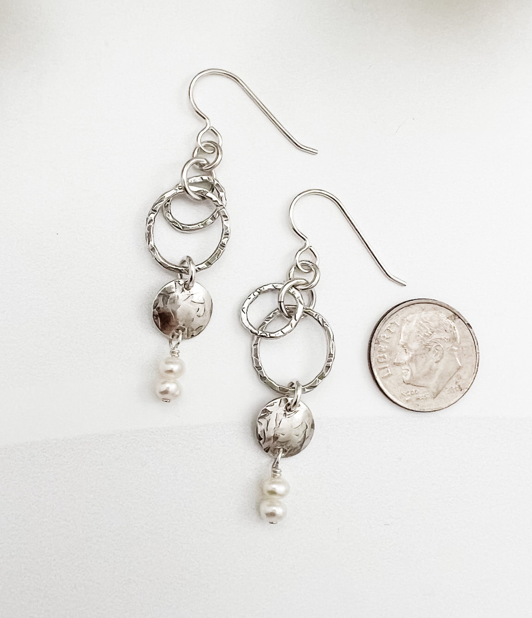 Sterling silver and pearl dangle earrings shown next to dime for scale, featuring textured hoops and luminous freshwater pearl drops, handmade by Dawn Carlson Designs