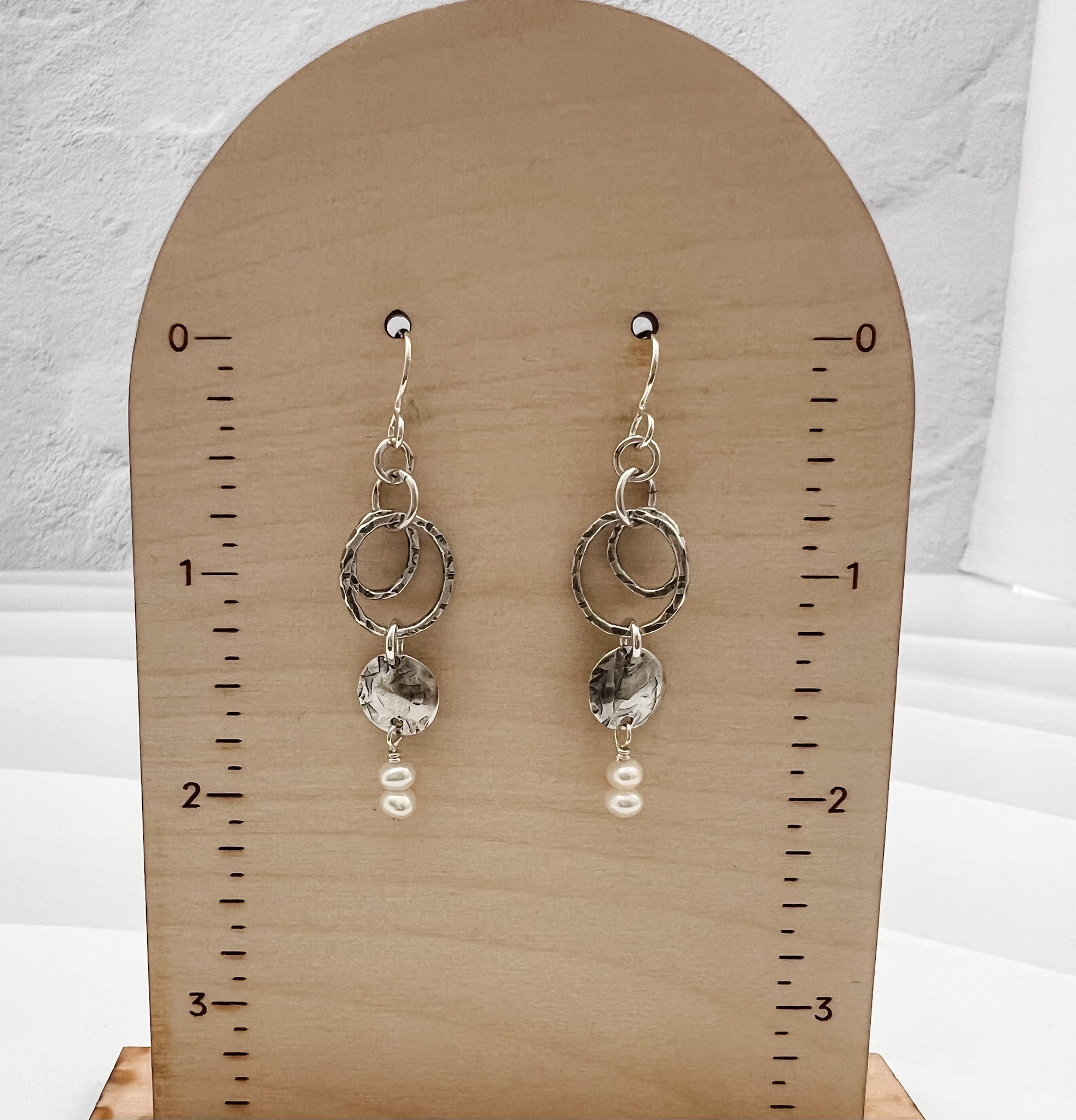 Caroline silver and pearl earrings displayed on wooden earring card showing 2-inch length, featuring hammered sterling silver circles and freshwater pearl accents