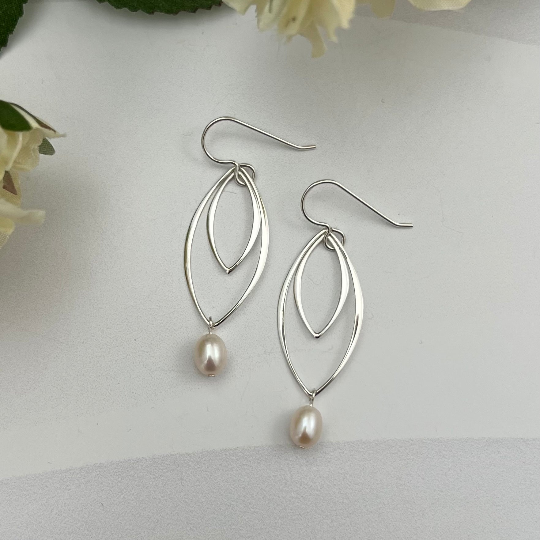 Double marquis sterling silver earrings with freshwater pearls by Dawn Carlson Designs, styled with white flowers on textured background