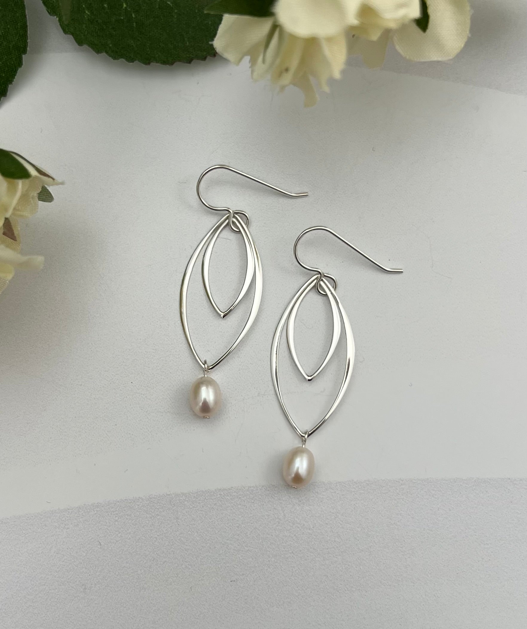 Double marquis sterling silver earrings with freshwater pearls by Dawn Carlson Designs, styled with white flowers on textured background