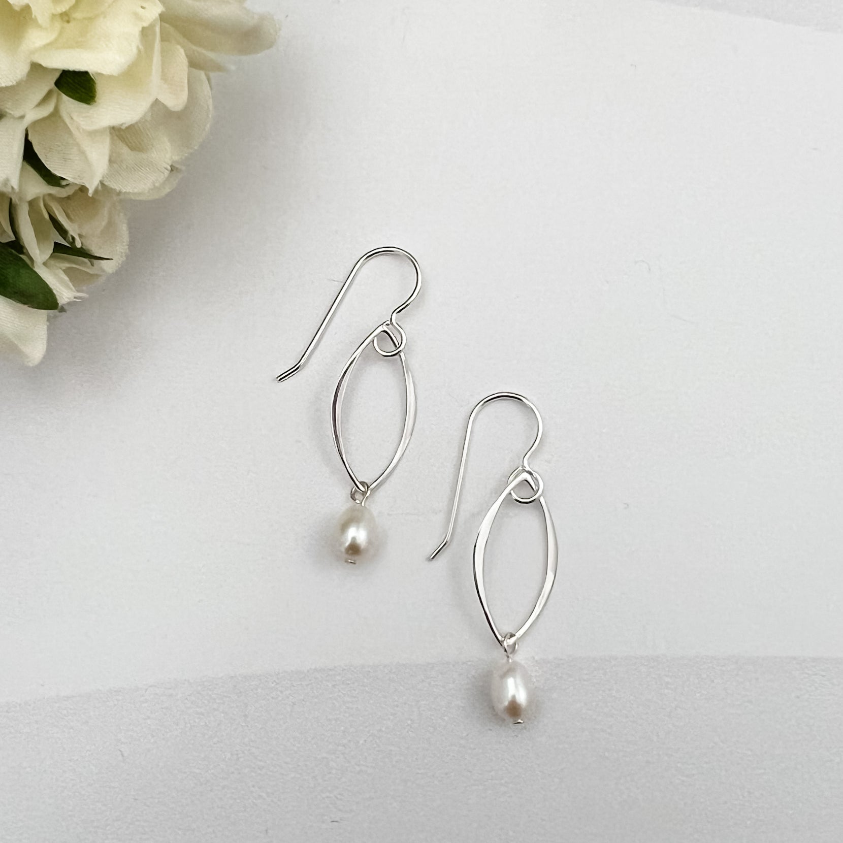 Marquis pearl drop earrings in sterling silver on white background with cream flower accent by Dawn Carlson Designs