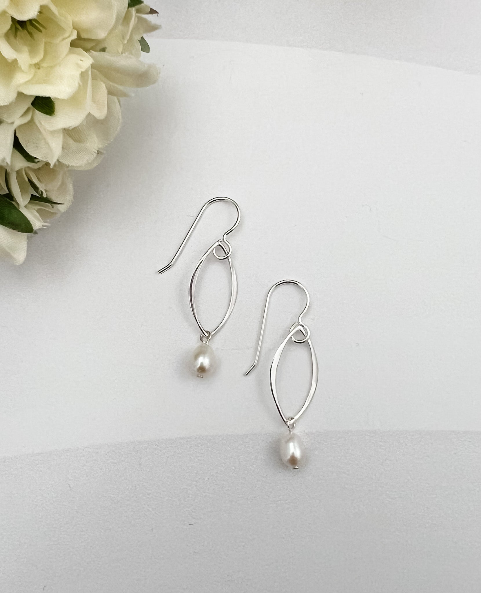 Marquis pearl drop earrings in sterling silver on white background with cream flower accent by Dawn Carlson Designs