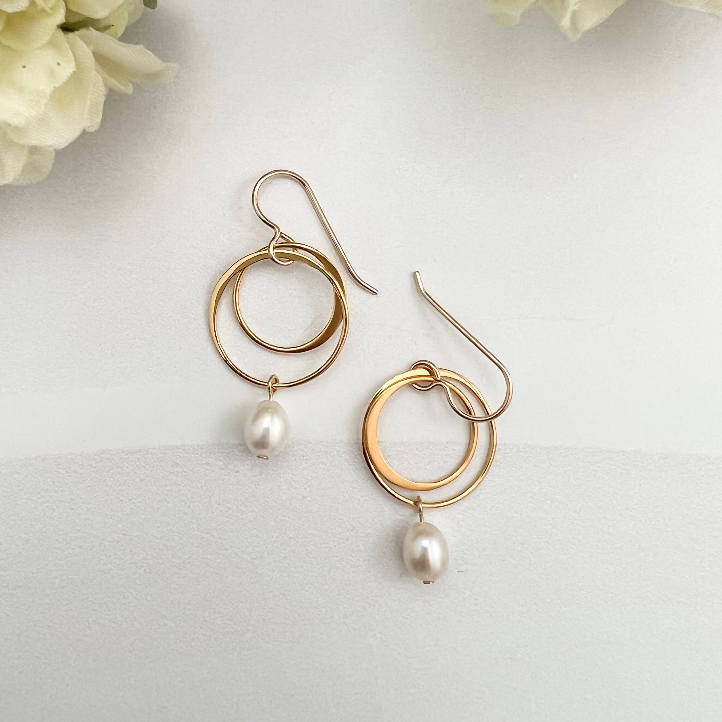 Gold vermeil double hoop earrings with freshwater pearl drops on white background with two flowers