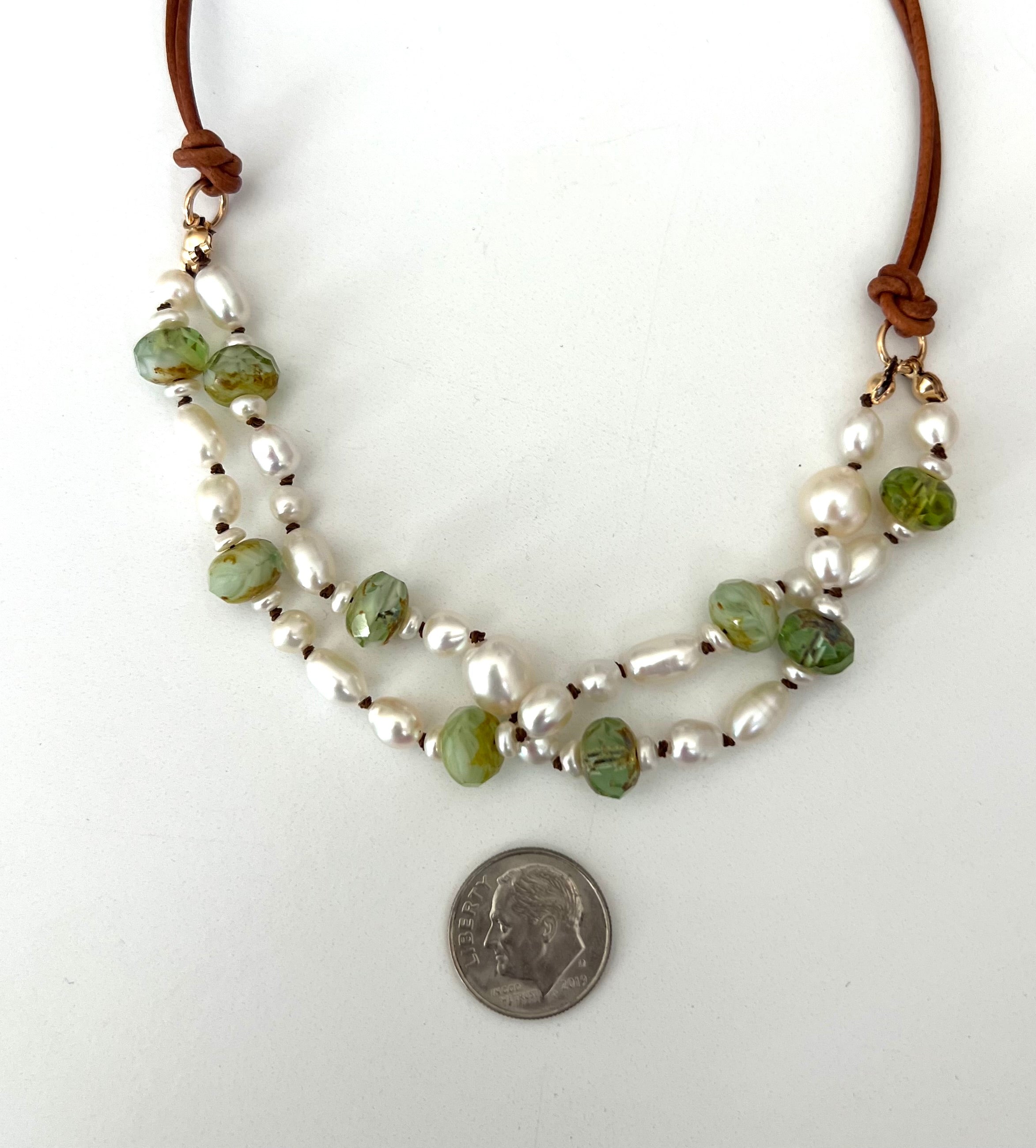 Double-strand freshwater pearl necklace on natural leather cord, accented with faceted green Czech glass beads and 14k gold filled jump rings, shown next to a dime for scale