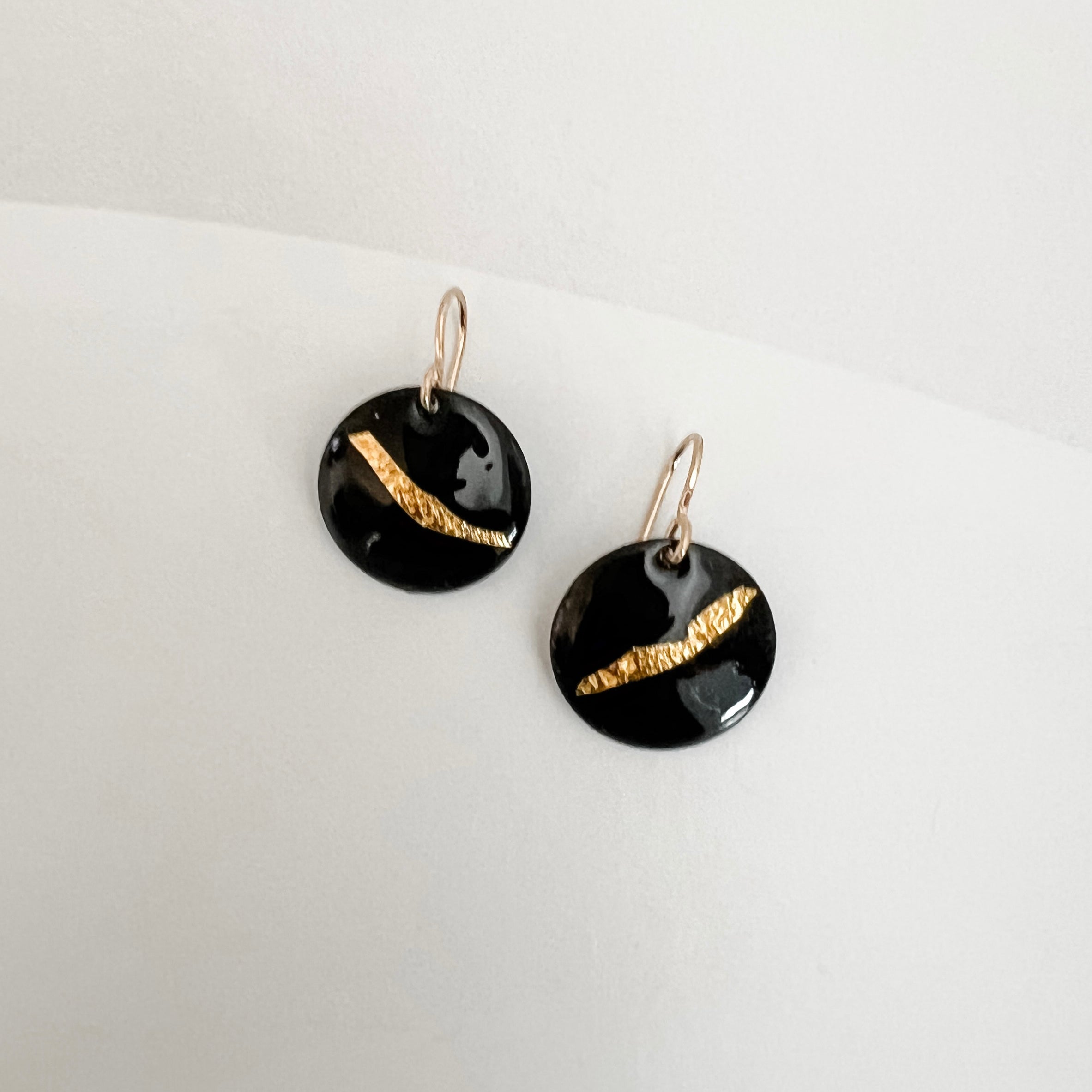 Close-up of black enamel drop earrings showing textured 24k gold foil sweep, handmade by Dawn Carlson Designs on a white background.