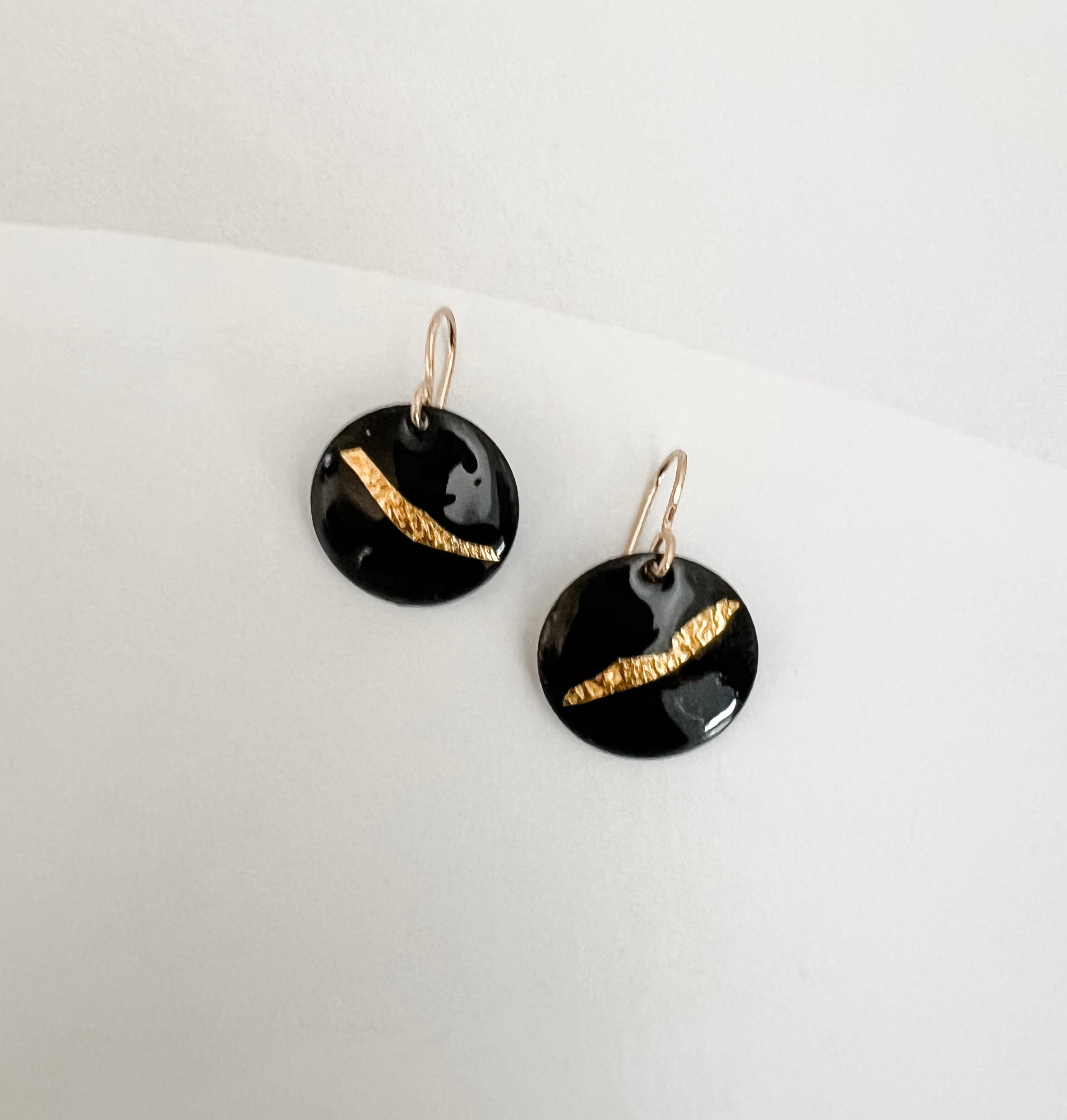 Close-up of black enamel drop earrings showing textured 24k gold foil sweep, handmade by Dawn Carlson Designs on a white background.