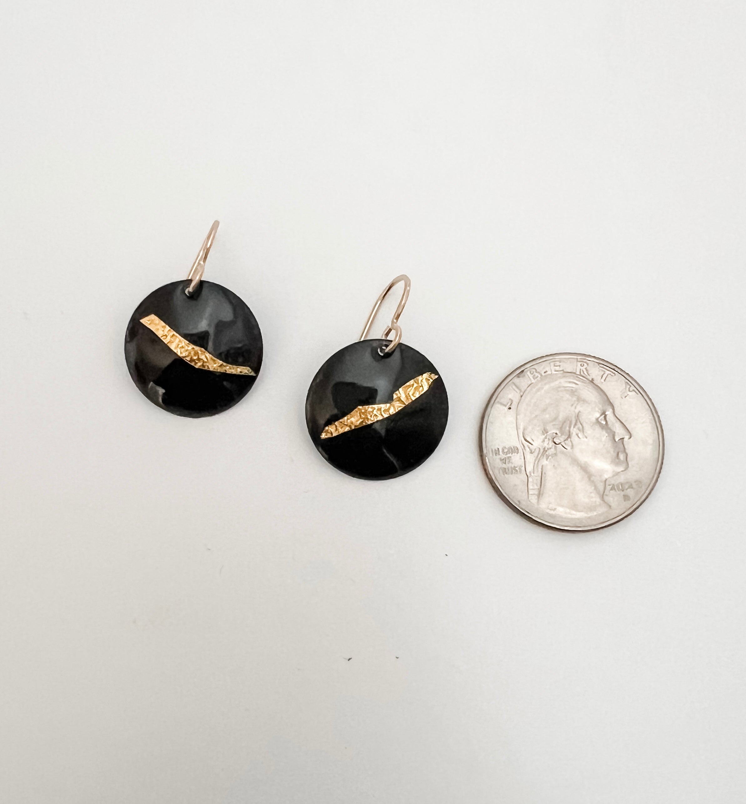 Black enamel and 24k gold foil disc earrings shown next to a quarter for scale, handcrafted by Dawn Carlson Designs