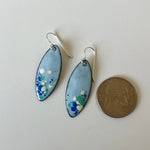 A pair of handmade enamel marquise drop earrings with light blue, green, and white speckled enamel and sterling silver fishhook wires, shown next to a US quarter for scale on a plain white surface.
