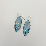 Handcrafted light blue enamel earrings with dark blue, cream, and seafoam splashes on sterling silver ear wires by Dawn Carlson Designs on a white background.