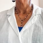 Close up of a woman wearing a hand knotted pearl lariat style necklace worn with a white linen blouse. Dawn Carlson Designs.