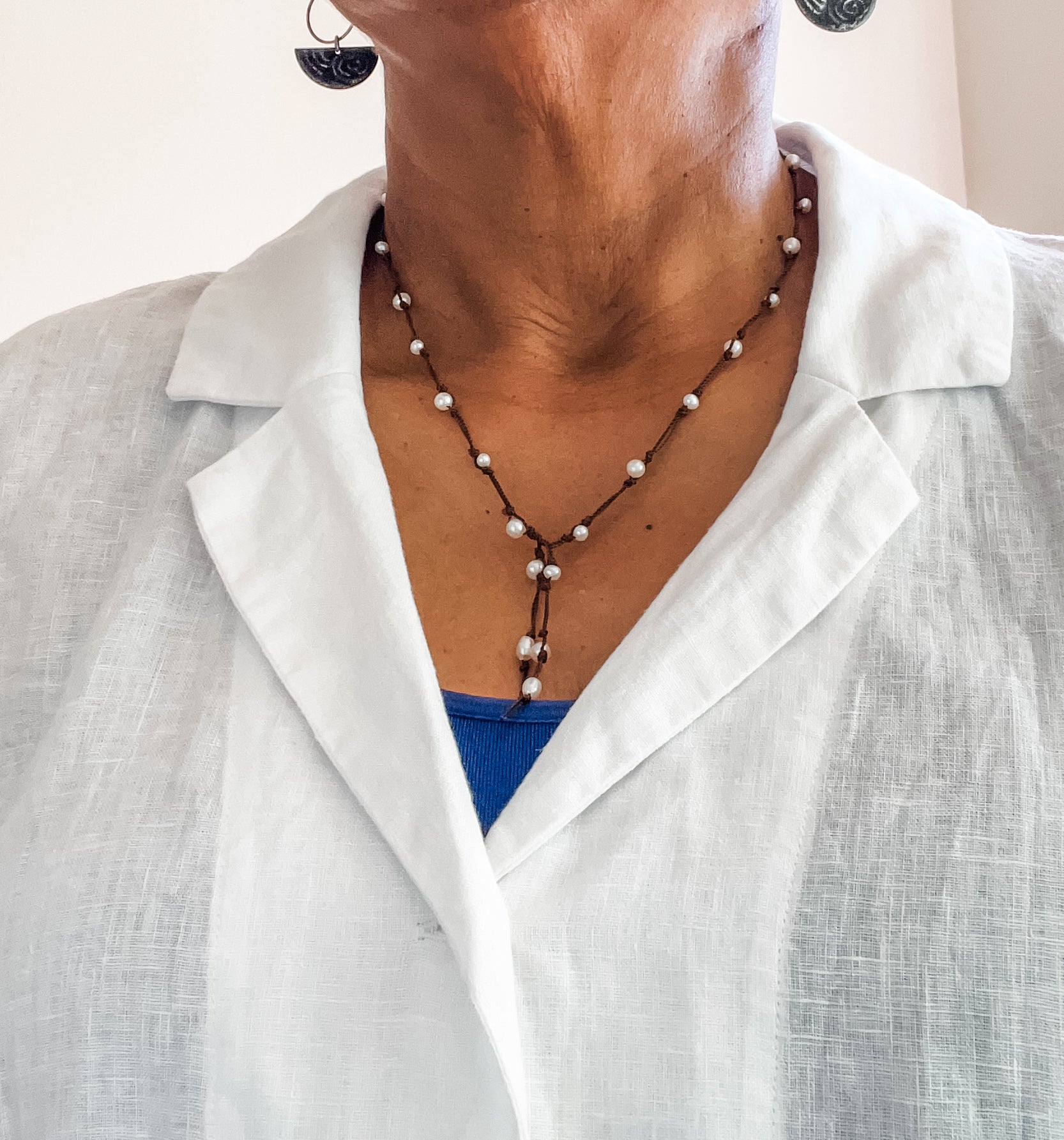 Close up of a woman wearing a hand knotted pearl lariat style necklace worn with a white linen blouse. Dawn Carlson Designs.