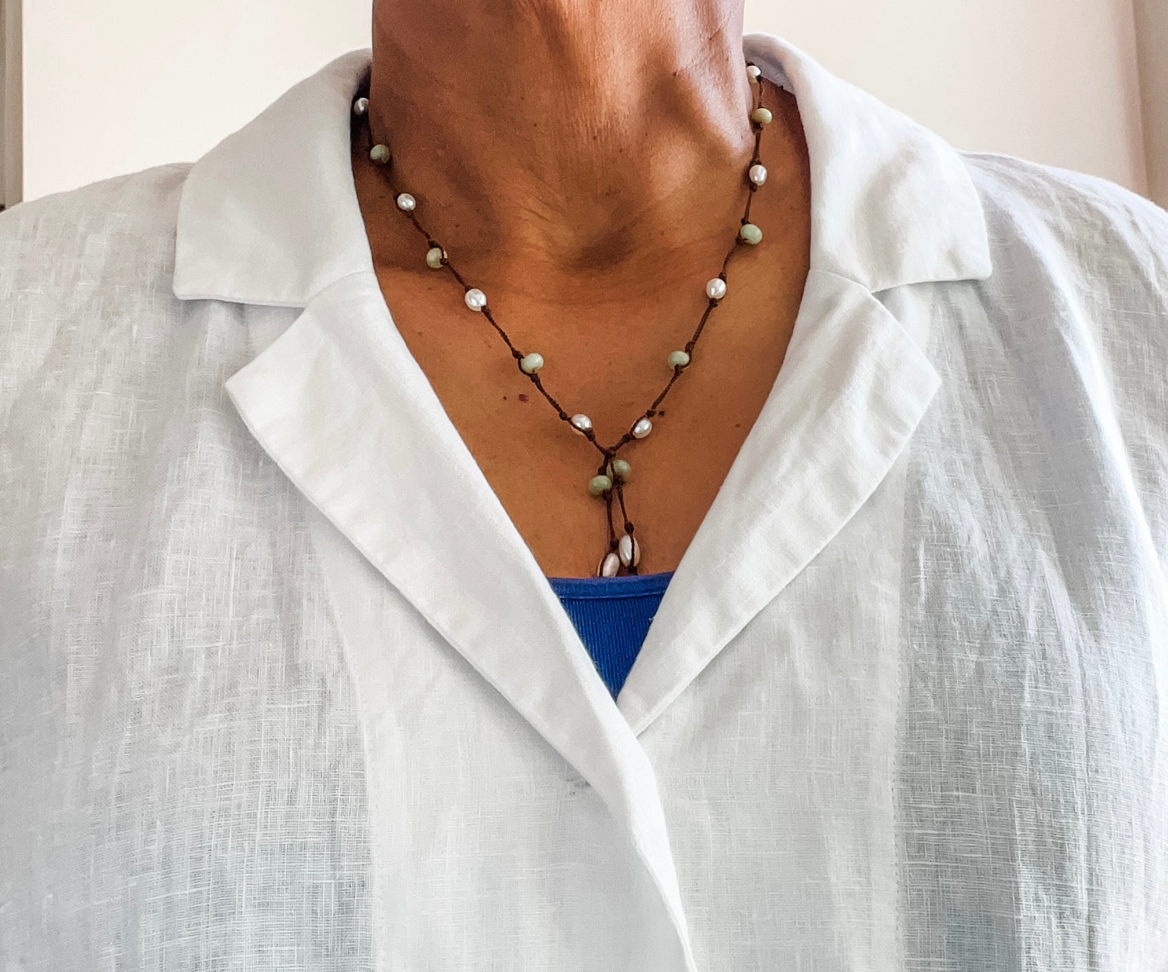 Pearl and peridot hand knotted lariat necklace shown on a person wearing a white linen blouse. Clasp free design.
