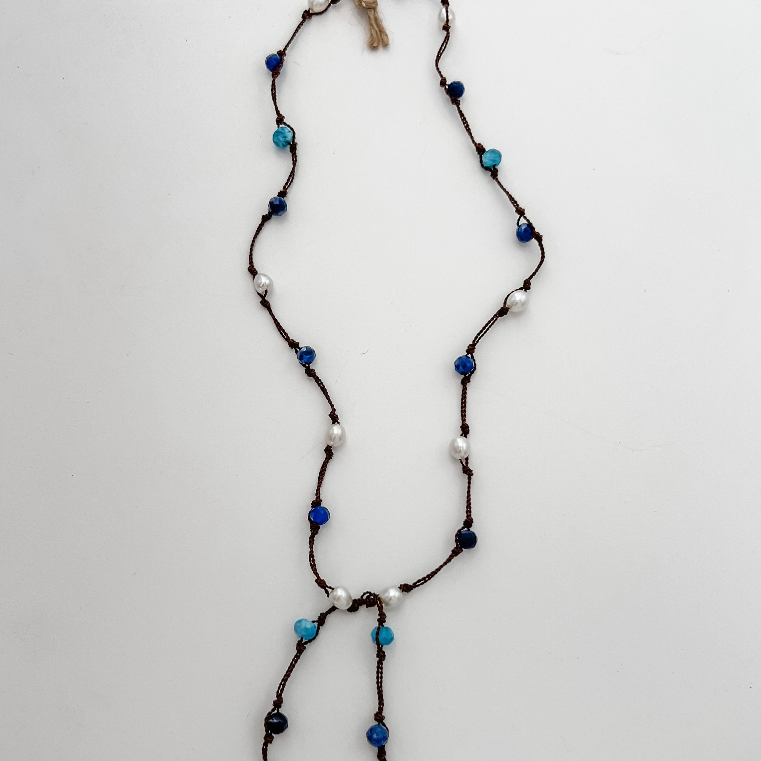 Apatite, sodalite and pearls knotted on brown cord with white background and branded tag.