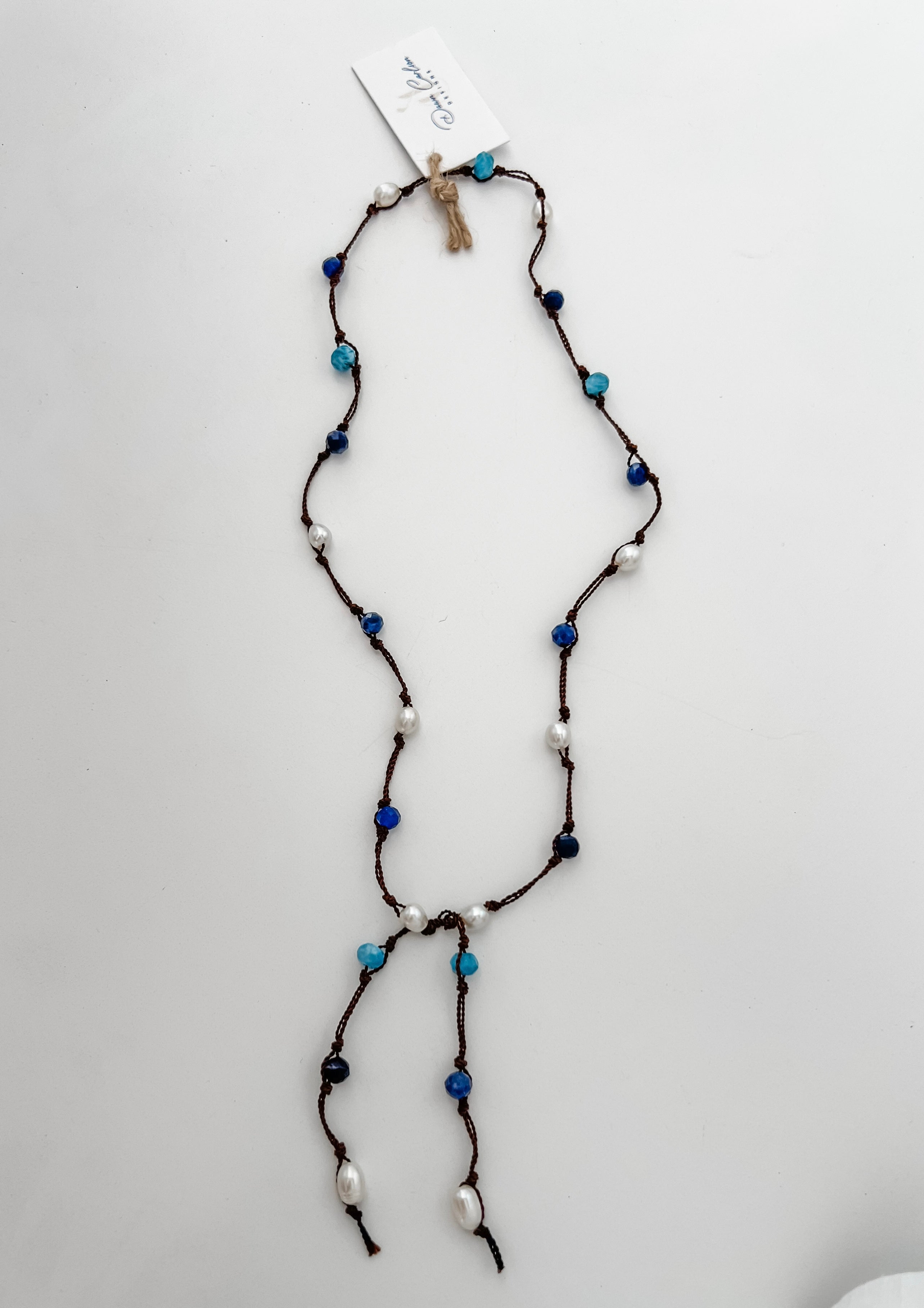 Apatite, sodalite and pearls knotted on brown cord with white background and branded tag.