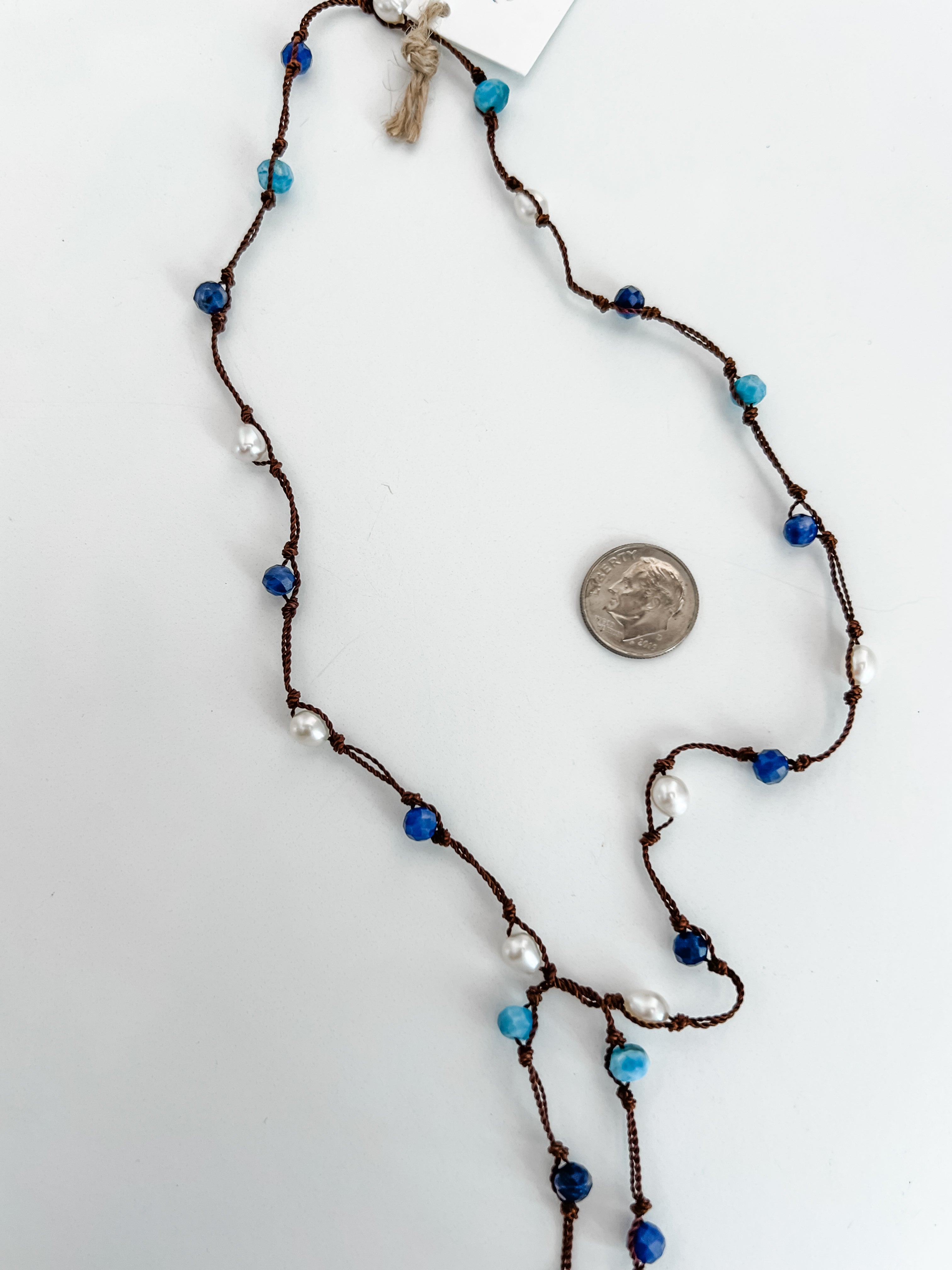 close up of hand knotted pearls, apatite and sodalite beads necklace. Lariat style, no clasp. Shown with a dime for reference on a white background.