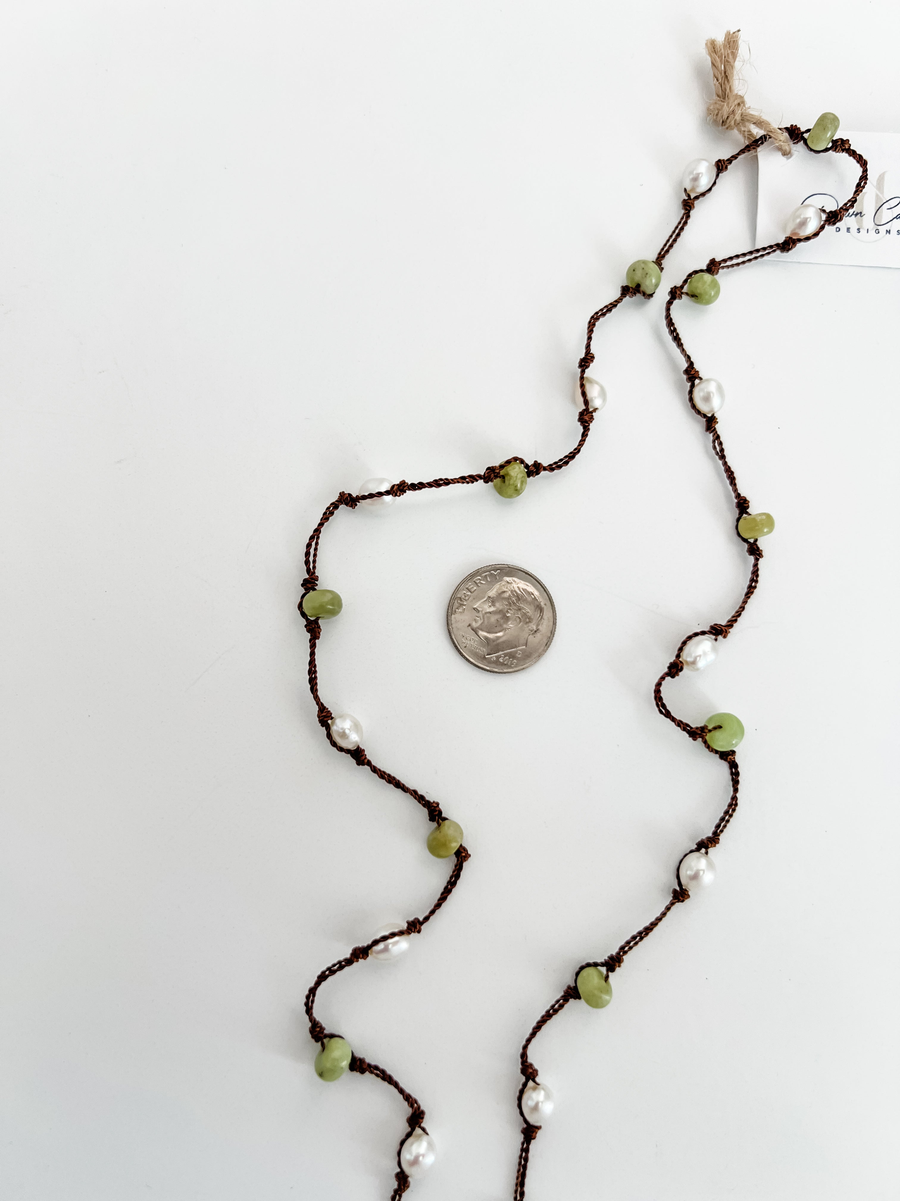 Close up of hand knotted freshwater pearls and peridot on nylon cord, artisan jewelry detail. Showing a dime next to the necklace for reference.