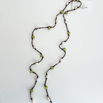 Hand knotted pearl and peridot lariat necklace laid out on a plain white background with a small, branded tag attached.