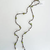 Hand knotted pearl and peridot lariat necklace laid out on a plain white background with a small, branded tag attached.