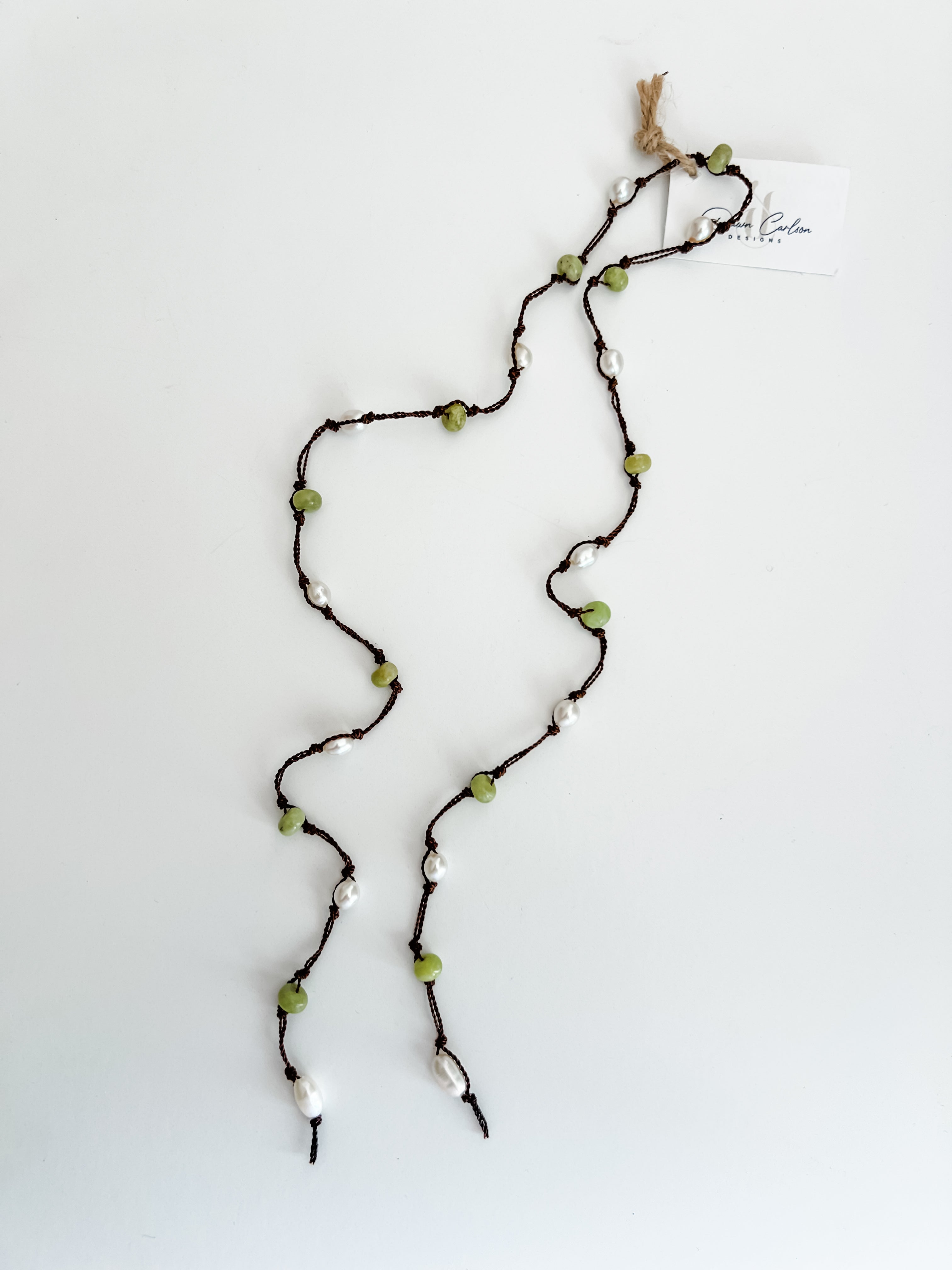 Hand knotted pearl and peridot lariat necklace laid out on a plain white background with a small, branded tag attached.