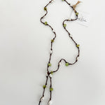 Hand knotted pearl and peridot lariat on brown nylon cord, laid out on a plain white background with a small, branded tag attached.
