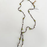 Hand knotted pearl and peridot lariat on brown nylon cord, laid out on a plain white background with a small, branded tag attached.