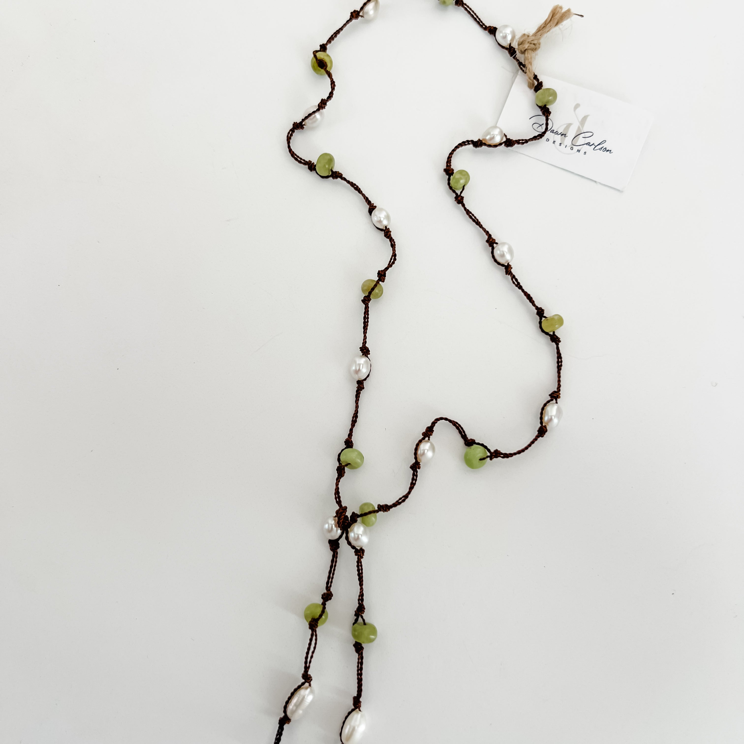 Hand knotted pearl and peridot lariat on brown nylon cord, laid out on a plain white background with a small, branded tag attached.