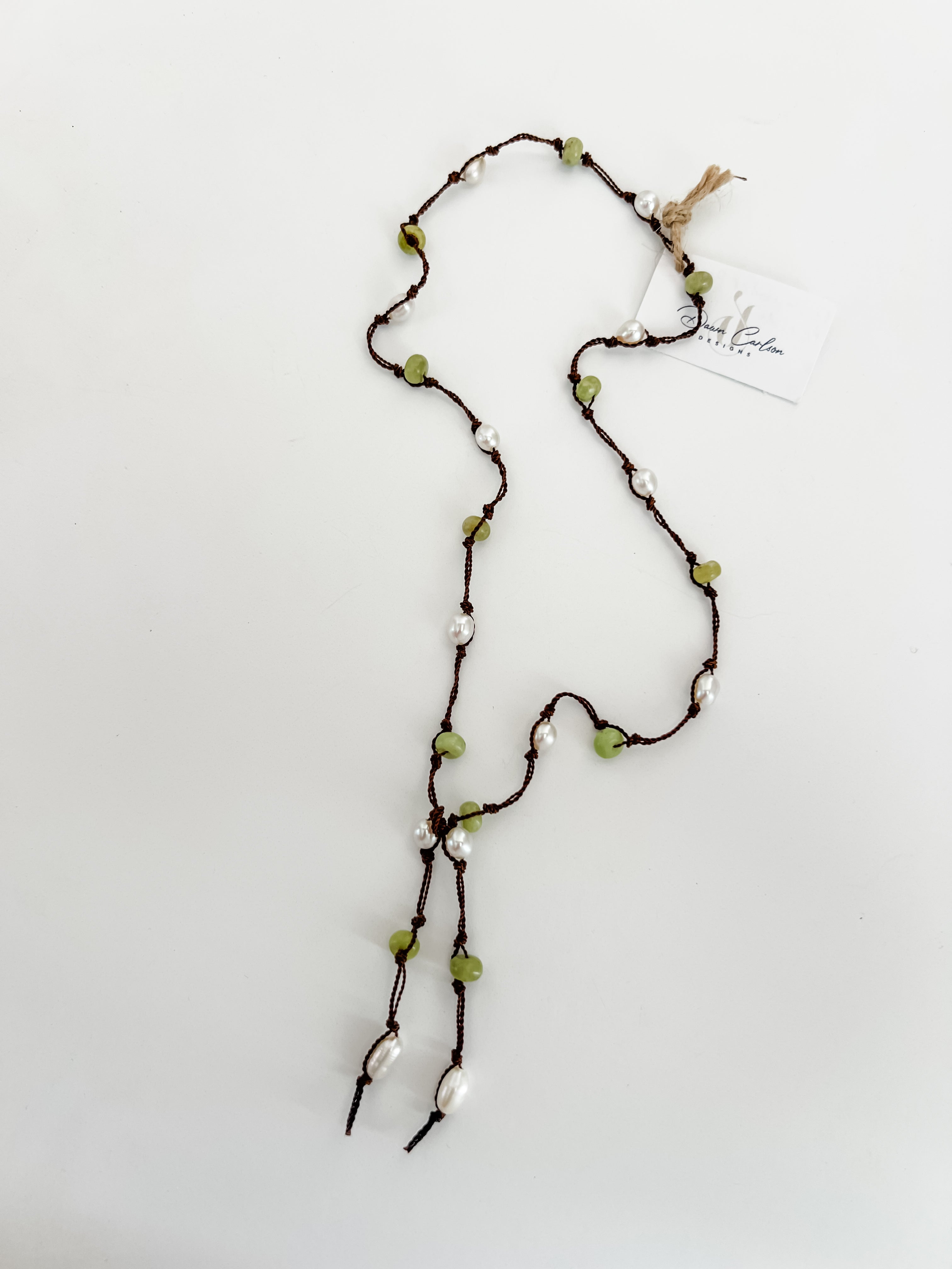 Hand knotted pearl and peridot lariat on brown nylon cord, laid out on a plain white background with a small, branded tag attached.
