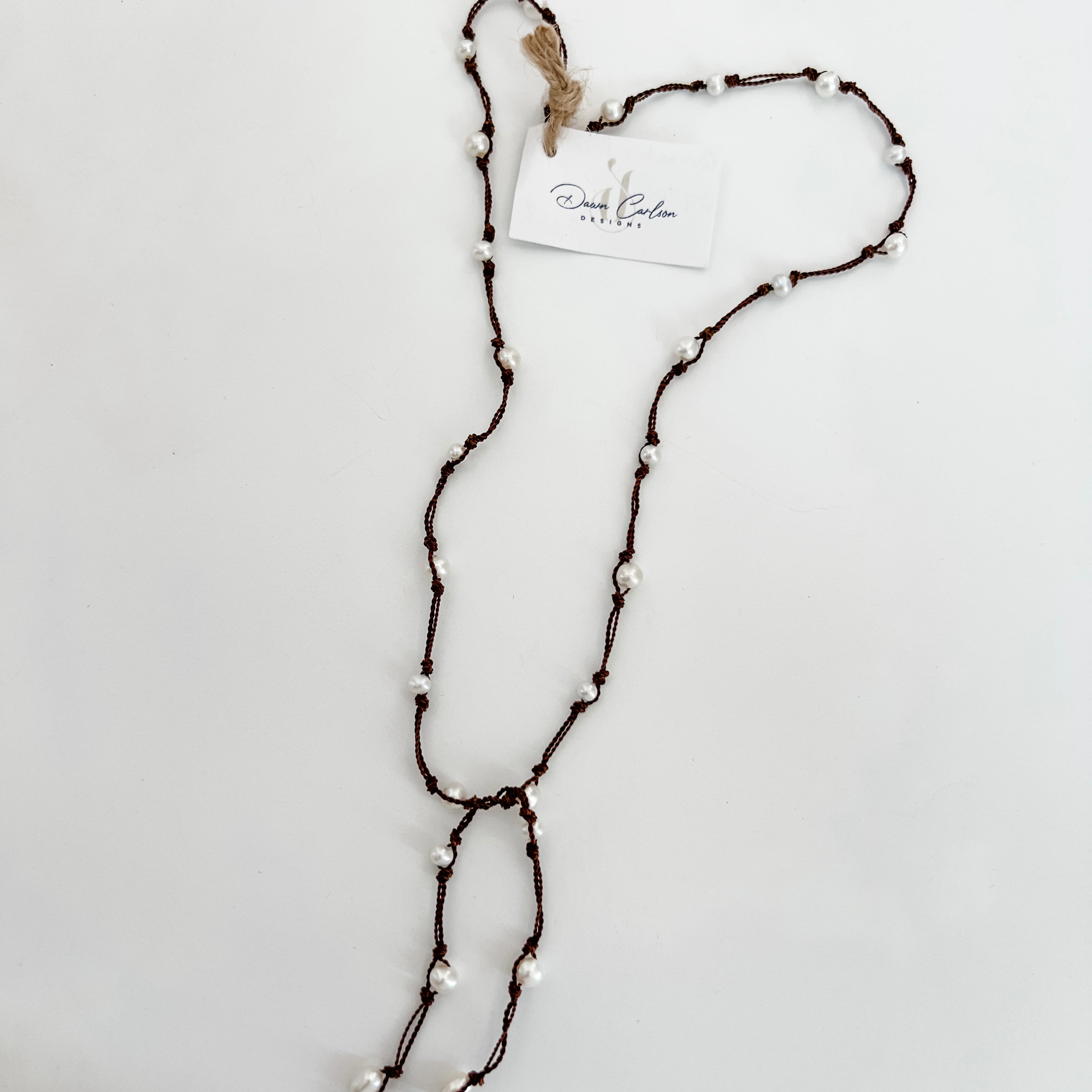 Freshwater pearls hand knotted on brown cord for a lariat necklace. Shown on a white background with a branded tag.