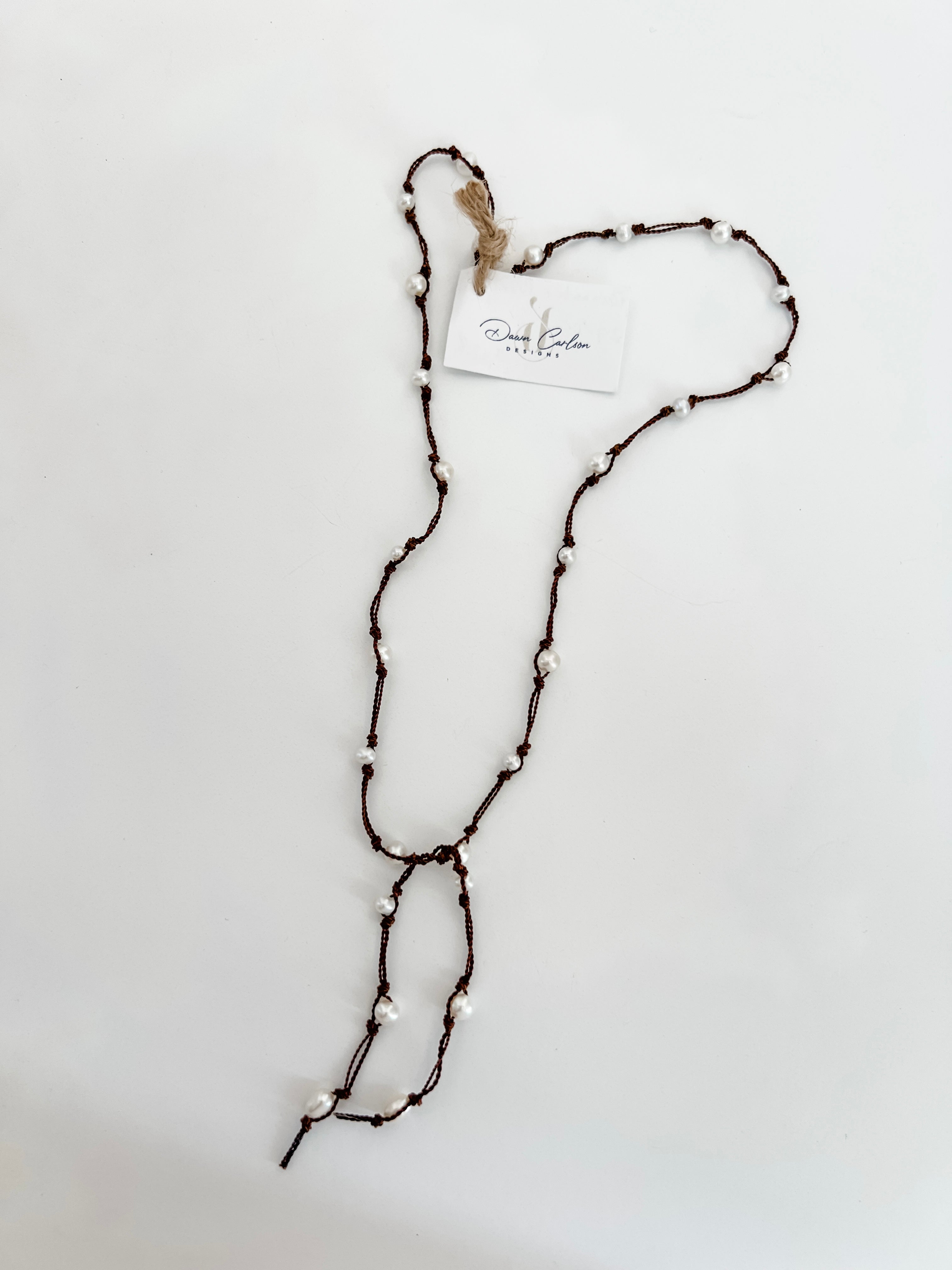 Freshwater pearls hand knotted on brown cord for a lariat necklace. Shown on a white background with a branded tag.